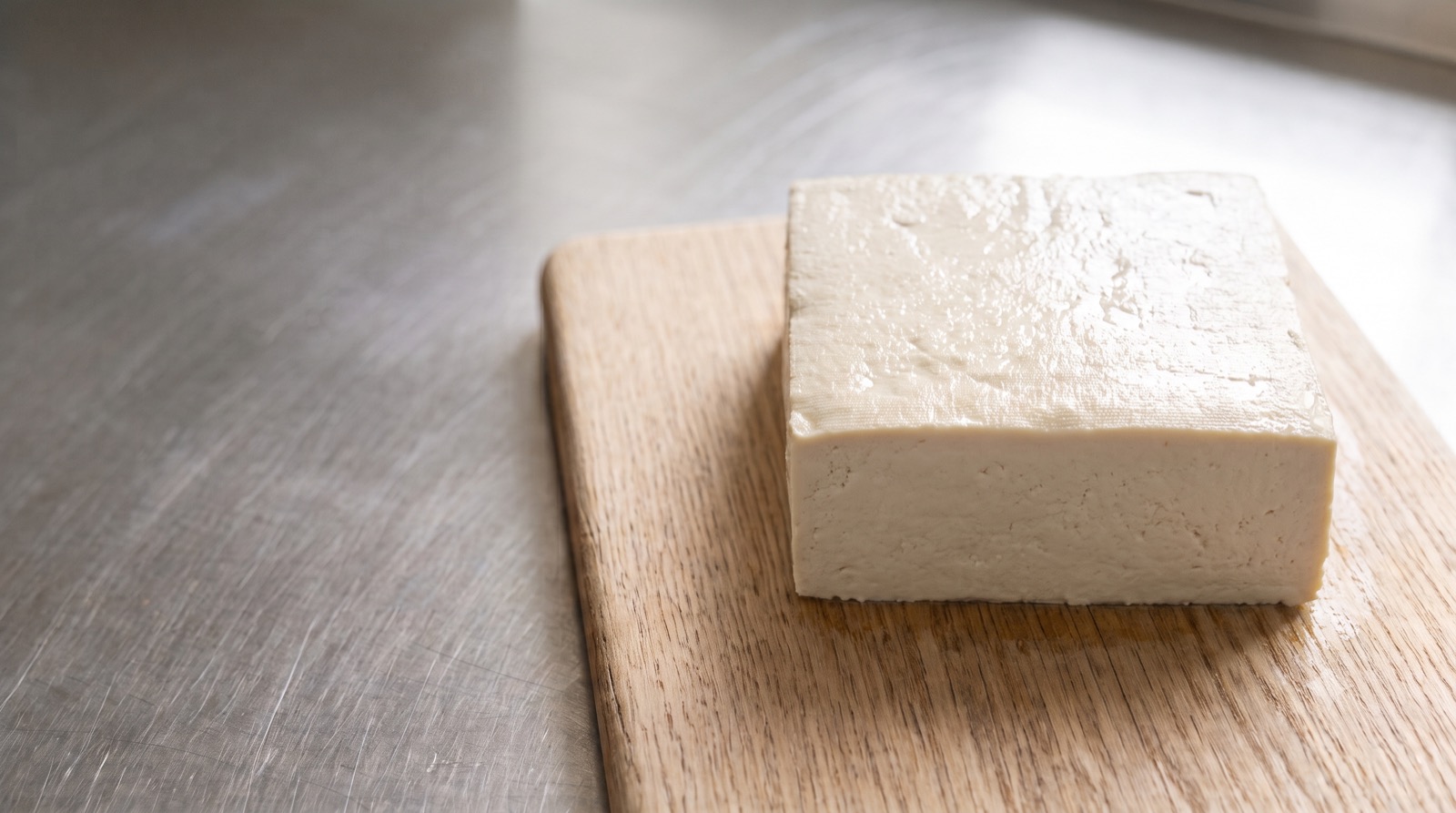 A fresh block of firm tofu on a wooden board